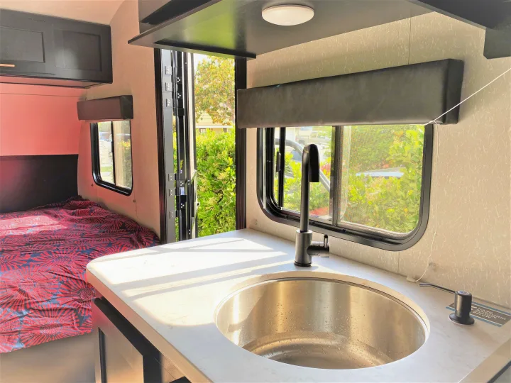 RV rental interior features a functional kitchen with a stainless steel sink, a comfortable bed, and scenic window views.. Forest River Cherokee Wolf Pup 2022