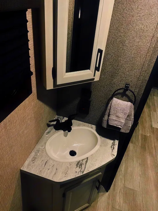 Compact RV rental bathroom with white sink, black faucet, gray textured walls, medicine cabinet, and towels.. jayco Jay feather 199mbs 2022