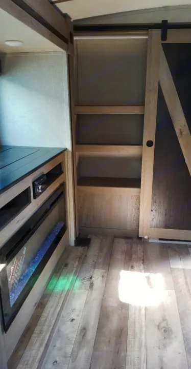 Inside an RV rental: features a sleek fireplace, media center, built-in shelves, and rustic barn door on wood-look flooring.. Keystone RV Outback 2021