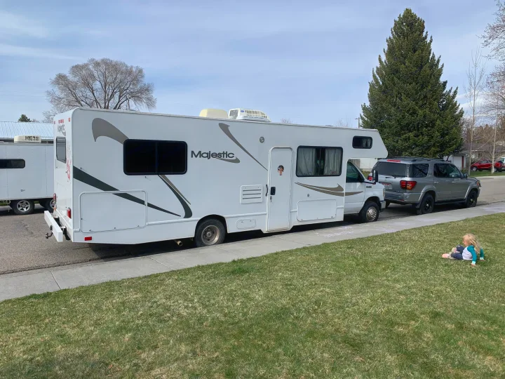 White Majestic RV rental parked on a street. A child sits on the sunny grass nearby, ready for adventure.. Other Other 2008