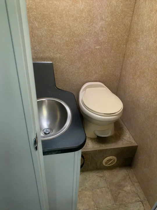 Explore our RV rental's compact washroom, featuring a white toilet, stainless steel sink, and tiled shower area.. Other Other 2008