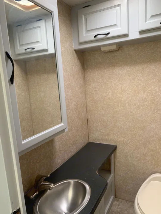 Inside an RV rental: a bathroom vanity with a stainless steel sink, black countertop, white cabinets, and mirror.. Other Other 2008