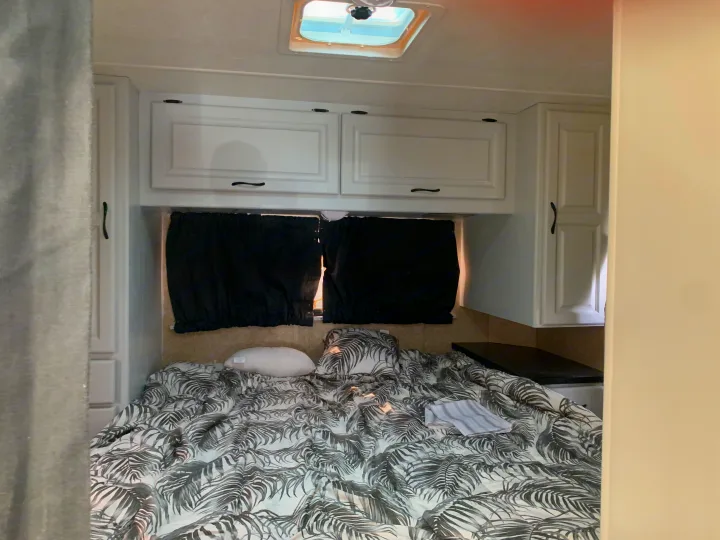 RV rental bedroom: bed with tropical palm-print bedding, white cabinets, and black window coverings.. Other Other 2008