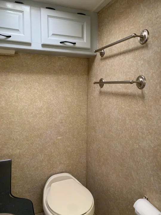 Compact RV rental bathroom interior, featuring beige textured walls, white cabinets, toilet, and shower curtain rods.. Other Other 2008