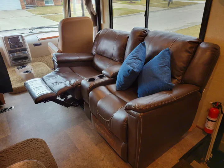 Spacious RV rental interior featuring a brown reclining leather loveseat with blue pillows & driver's area.. Winnebago Vista 2018