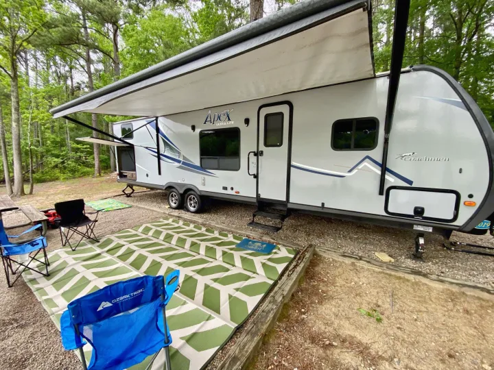 Perfect campsite setup! A gray RV rental with a deployed awning, green mat, and blue chairs, surrounded by trees.. Coachmen Other 2019