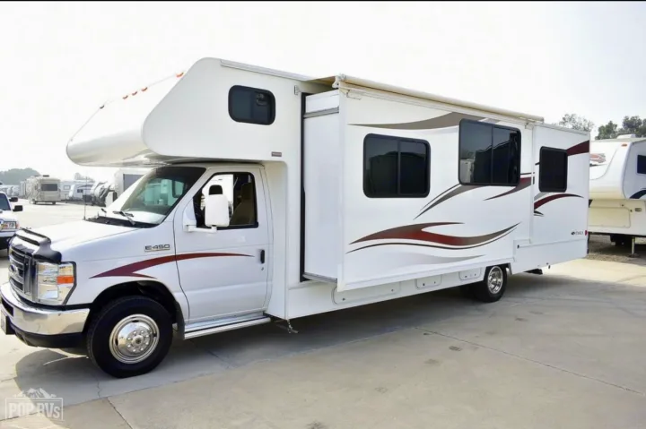 A white Class C RV rental with an extended slide-out section and brown graphics, parked on concrete.. Itasca Spirit 2014
