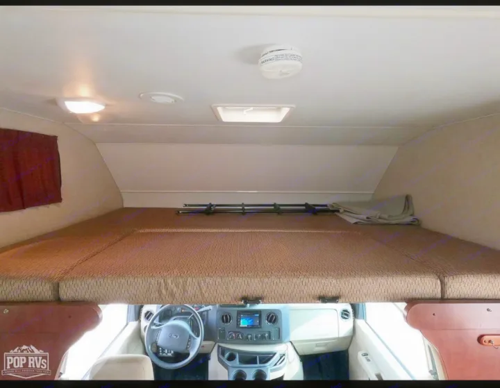 View of an RV rental's over-cab bunk bed, showing dashboard, ceiling lights, and smoke detector.. Itasca Spirit 2014