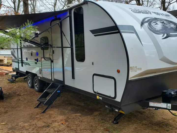 Grey Wolf travel trailer RV rental, featuring an extended awning with blue lights and entry steps, ready for adventure.. Forest River Cherokee Grey Wolf 2021