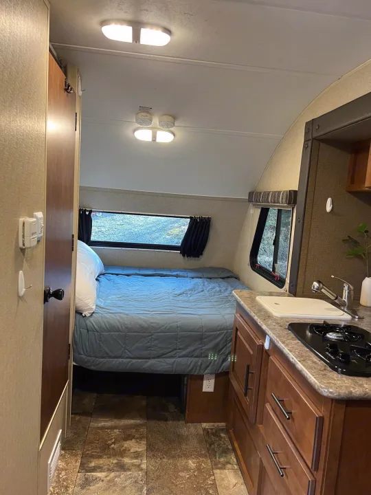 Cozy RV rental interior featuring a bed, compact kitchen with sink and stovetop, and scenic window views.. Forest River R-Pod 2015