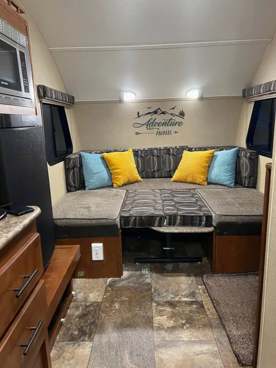 RV rental interior featuring a cozy dinette with U-shaped seating, "Adventure Awaits" decor, microwave, and fridge.. Forest River R-Pod 2015