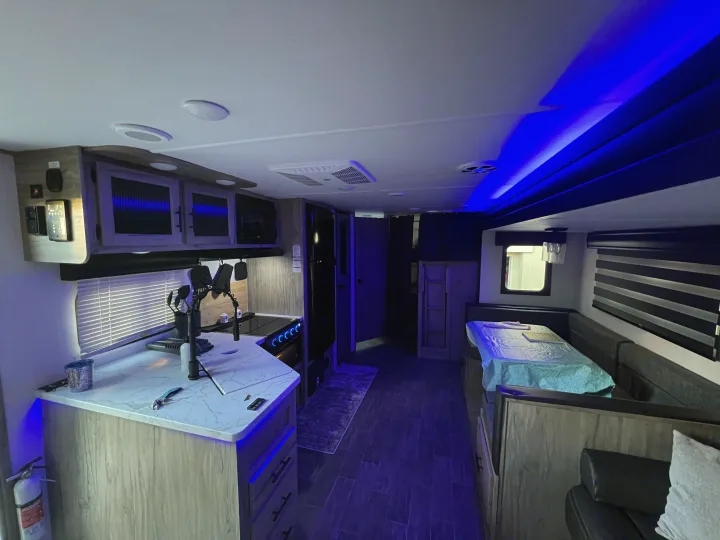 Modern rv rental interior showcasing a well-equipped kitchen, dining area, and ambiance from blue LED lighting.. Forest River Cherokee Alpha Wolf 2022