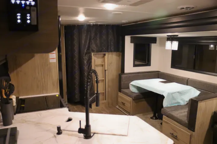 RV rental interior: kitchen counter with sink, U-shaped dinette with blue tablecloth, and a curtained bunk area.. Forest River Cherokee Alpha Wolf 2022