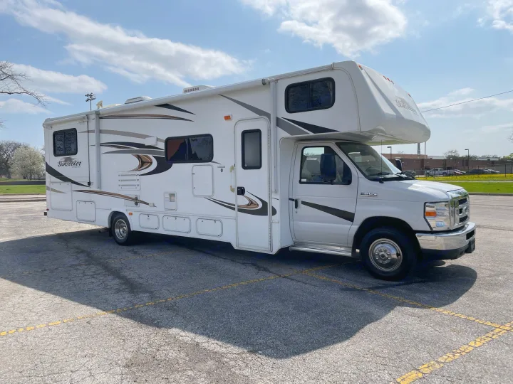 A white Sunseeker Class C RV rental parked on an asphalt lot under a partly cloudy sky.. Forest River Sunseeker 2013