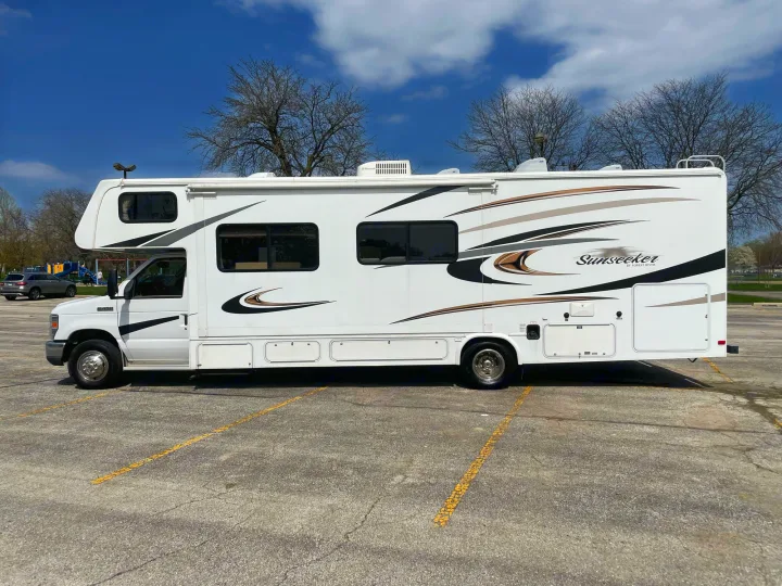 White Sunseeker Class C RV rental parked outdoors, featuring distinctive brown and gold stripes. Perfect for travel adventures.. Forest River Sunseeker 2013