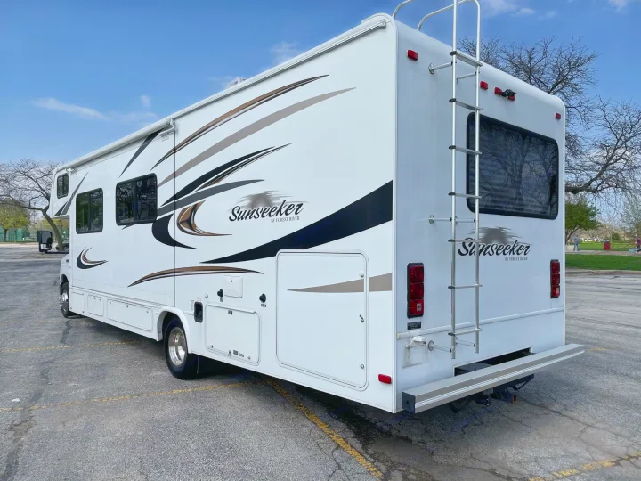 Sunseeker Class C RV, perfect for rv rental, showing its side, storage, rear ladder, & unique graphics.. Forest River Sunseeker 2013