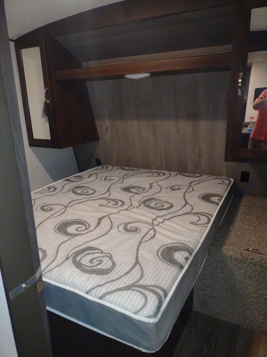 RV rental bedroom showcasing a patterned mattress, dark wood-grain walls, and a built-in nightstand.. Keystone Springdale 2020