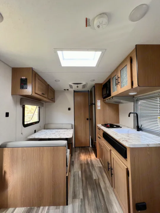 Modern RV rental interior, featuring a kitchen, dinette, and light wood cabinetry, ready for your trips.. Forest River Prime Time Avenger LT 16FQ 2022
