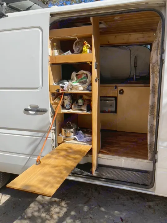 This RV rental shows a camper van interior with custom storage, kitchenette, and a handy pull-out table.. Dodge Sprinter 2003