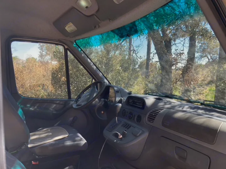 A spacious RV rental van cockpit. Features driver's seat, dashboard, & natural scenery visible through large windows.. Dodge Sprinter 2003