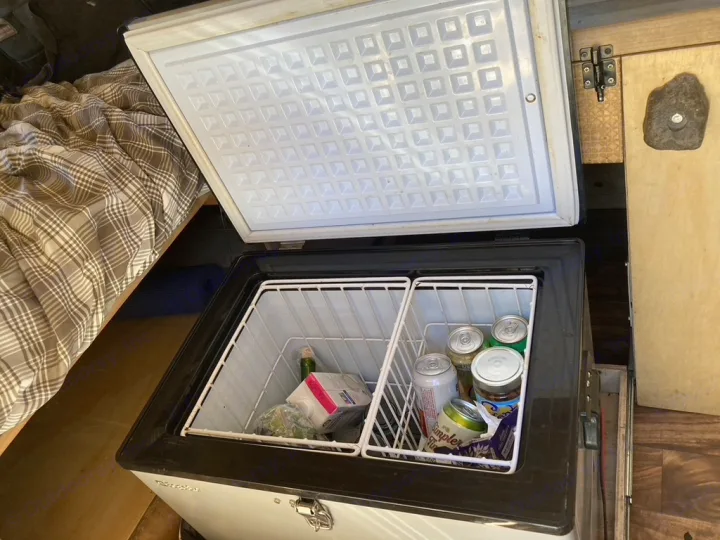 This RV rental's open chest cooler shows food & drinks, providing mobile storage next to the bed.. Dodge Sprinter 2003