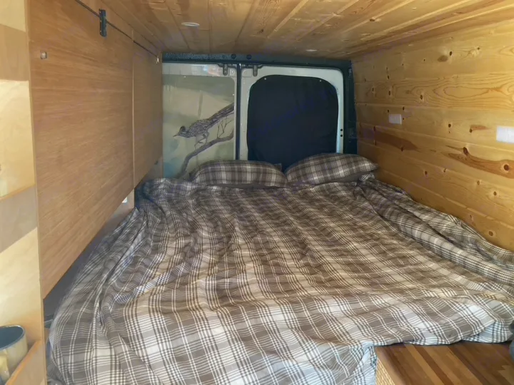 This **RV rental** features a cozy sleeping area with plaid bedding, wood-paneled walls, and roadrunner artwork.. Dodge Sprinter 2003