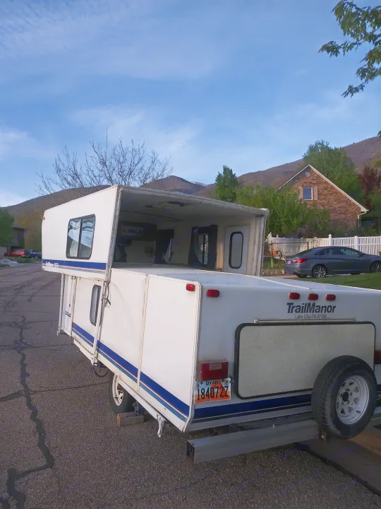 Open TrailManor pop-up RV rental with Utah plates, parked on a road by mountains.. K-Z Manufacturing Coyote 2002