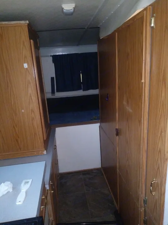 RV rental kitchen: wood grain cabinets, grey counter with utensil, dark tiled backsplash, & window with blinds.. K-Z Manufacturing Coyote 2002