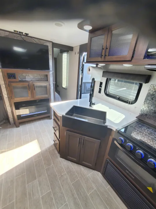 Modern RV rental kitchen with a large sink and stove, plus living area with TV & fireplace. Modern comfort.. Forest River Cherokee Grey Wolf 2021
