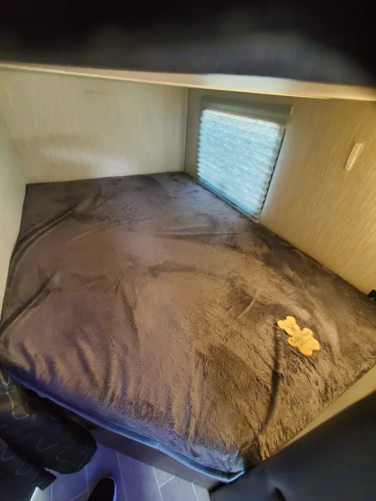 Bunk bed in an RV rental, featuring a plush grey blanket, window with blinds, and a "Teddy Bear Bunk Series" cutout.. Forest River Cherokee Grey Wolf 2021