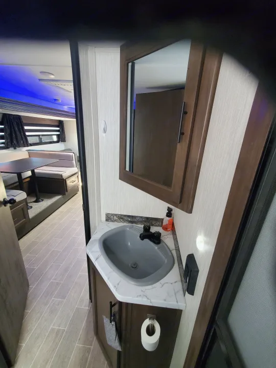 Explore this modern RV rental interior featuring a bathroom vanity, sleek living area with a dinette, and ambient blue lighting.. Forest River Cherokee Grey Wolf 2021