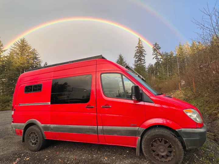 Red RV rental van parked outdoors, beneath a stunning double rainbow. Ready for adventure!. Freightliner Sprinter 2011