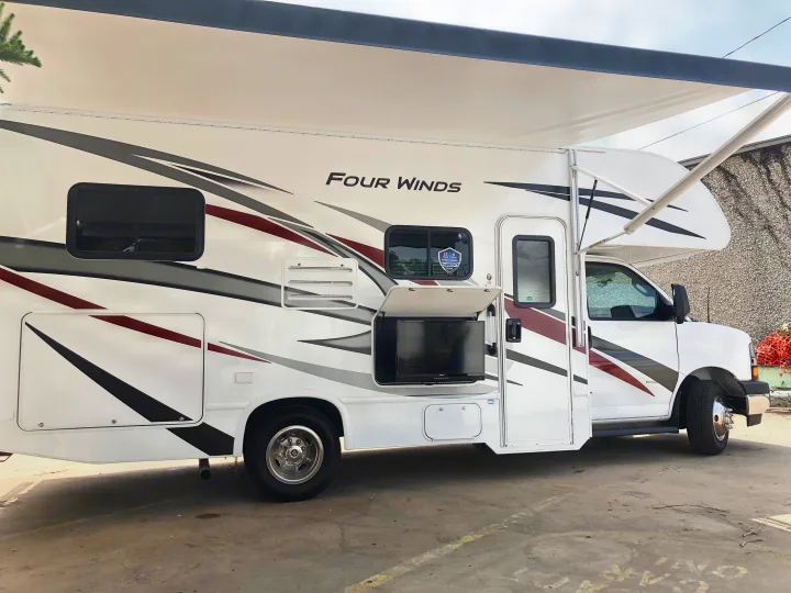 Spacious Four Winds RV rental, parked outdoors, featuring an extended awning and an exterior TV compartment.. Thor Four Winds 2022