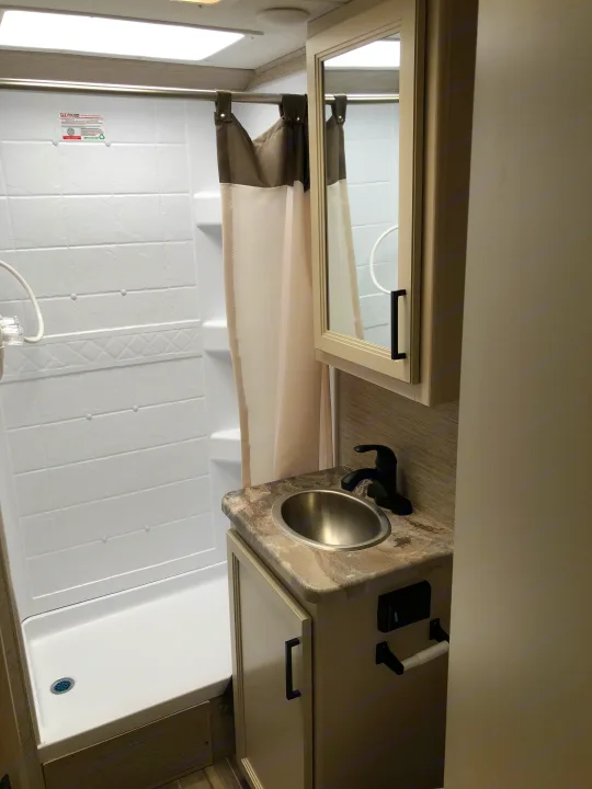 Clean and compact RV rental bathroom featuring a shower stall, modern sink vanity, and mirror.. Thor Four Winds 2022