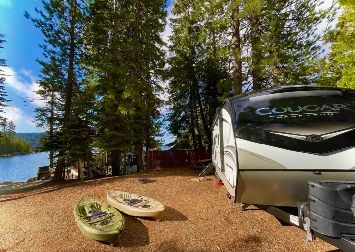 This lakeside RV rental offers a perfect camping setup with a modern trailer, two kayaks, and towering pine trees by the water.. Keystone Cougar Half-Ton 2022