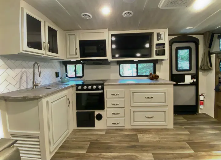 Explore this modern RV rental kitchen. Features light cabinetry, sink, microwave, oven, and TV for comfortable travels.. Keystone Cougar Half-Ton 2022