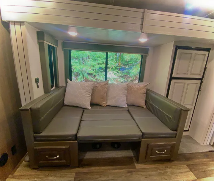 This RV rental features a comfortable dinette with grey cushions, a forest view window, and built-in storage.. Keystone Cougar Half-Ton 2022