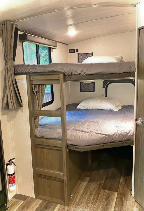 Explore a comfy RV rental bunk bed setup. This camper interior features two sleeping tiers & a window, ideal for families.. Keystone Cougar Half-Ton 2022