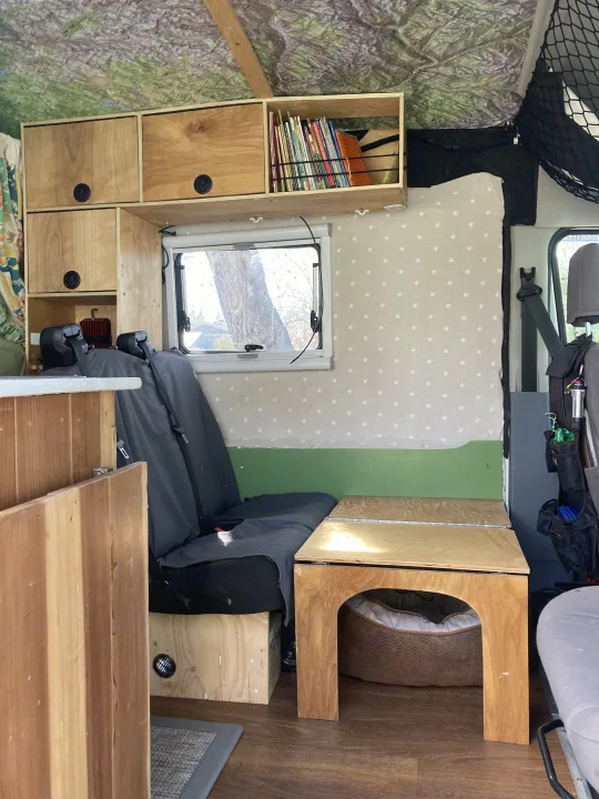 RV rental interior: Custom wood storage, bench seat, dog bed, and map-covered ceiling in a cozy camper van living space.. Ford Transit Custom 2015