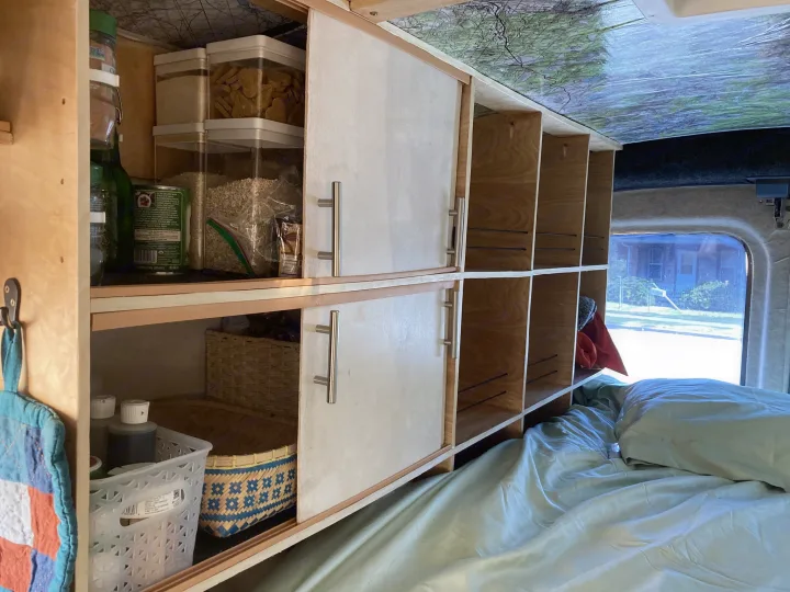 Custom RV rental interior with organized storage shelves, sliding doors, and a cozy bed for travel adventures.. Ford Transit Custom 2015