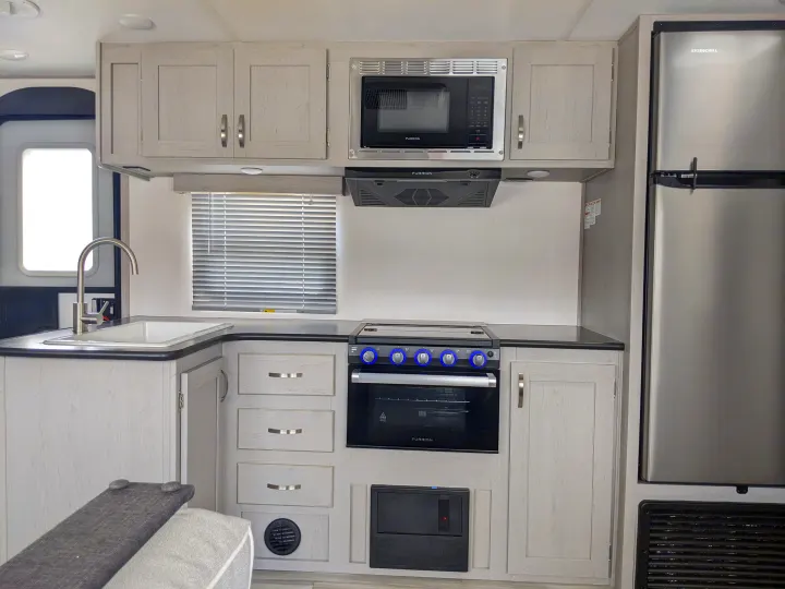 Bright, modern RV rental kitchen. Light wood cabinets, stainless steel sink, Furrion oven/microwave, and Everchill fridge.. Other Other 2022