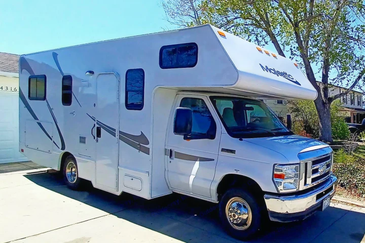 White Class C RV rental with gray graphics parked in a sunny driveway, ready for travel adventures.. Thor Majestic 2015