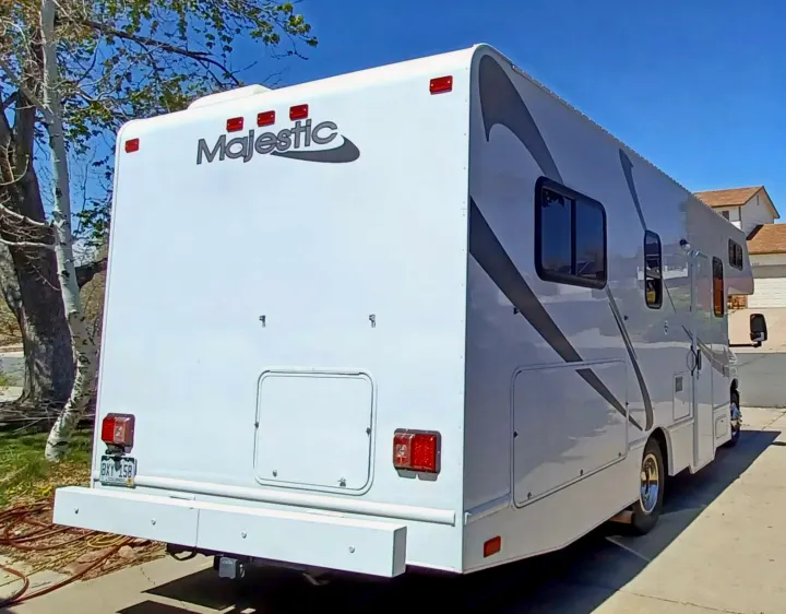 A white Majestic RV rental is seen from its rear and side, featuring gray stripes. It's parked outdoors, ready for camping.. Thor Majestic 2015