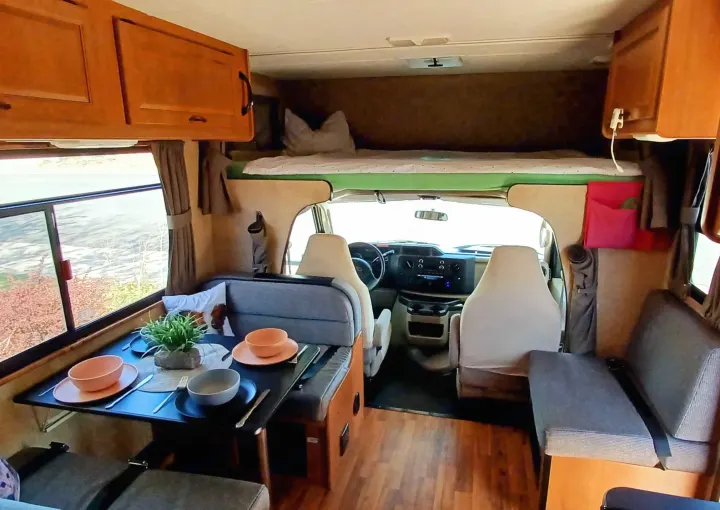 Functional rv rental interior with a laid dining table, an overhead bunk, and front cab seats, offering compact living.. Thor Majestic 2015