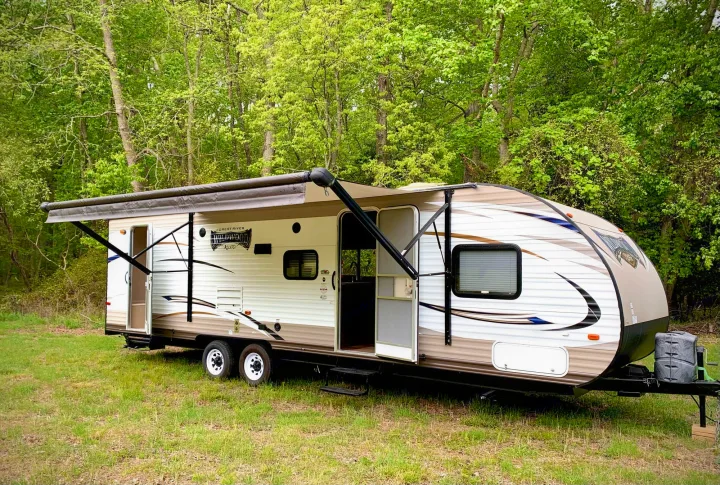 RV rental: A beige travel trailer with extended awning is ready on grass, backed by lush trees.. Forest River Wildwood X-Lite 2016