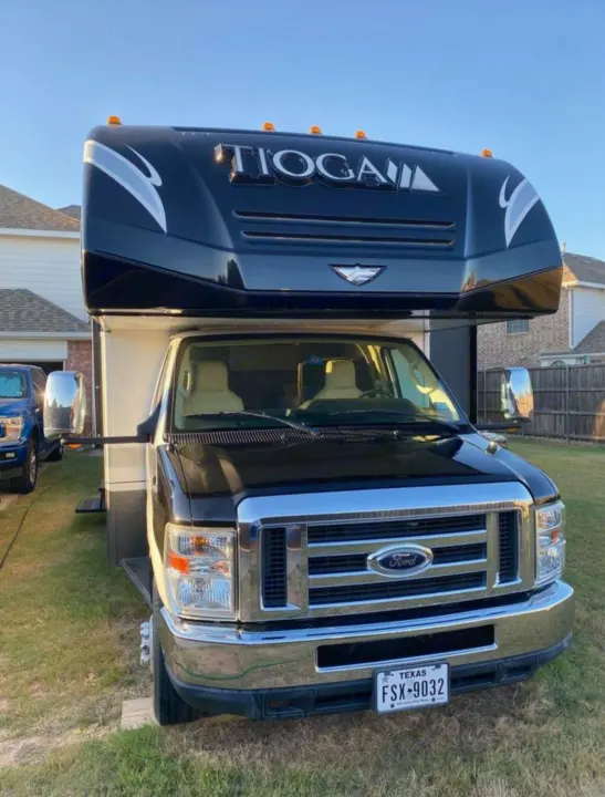 A sleek black Tioga Class C RV motorhome on a Ford chassis is parked in a yard. Your ideal RV rental awaits!. Tioga Tioga Motorhome 2012