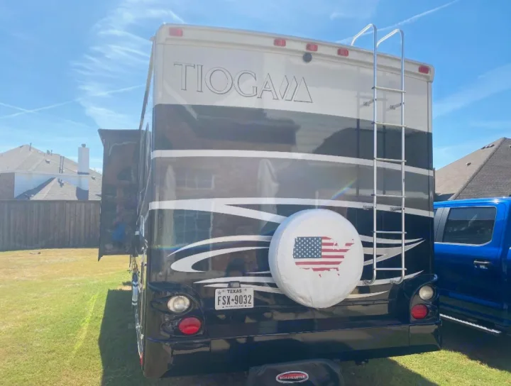 Rear view of a black & tan Tioga RV rental, showing its ladder and patriotic spare tire cover, parked on grass.. Tioga Tioga Motorhome 2012