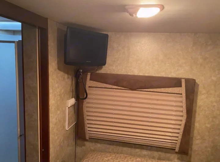 Compact RV rental interior with a wall-mounted TV, window blinds, and bed. Ready for your travels.. Tioga Tioga Motorhome 2012