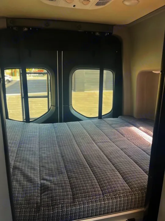 RV rental interior: A neatly made gray bed fills the back, visible through large rear windows.. Winnebago Revel 2022