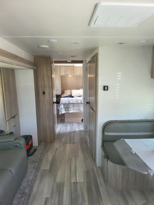 RV rental interior: Modern living area with grey seating and wood-look floor, leading to a cozy bedroom.. Winnebago Minnie Winnie 2022